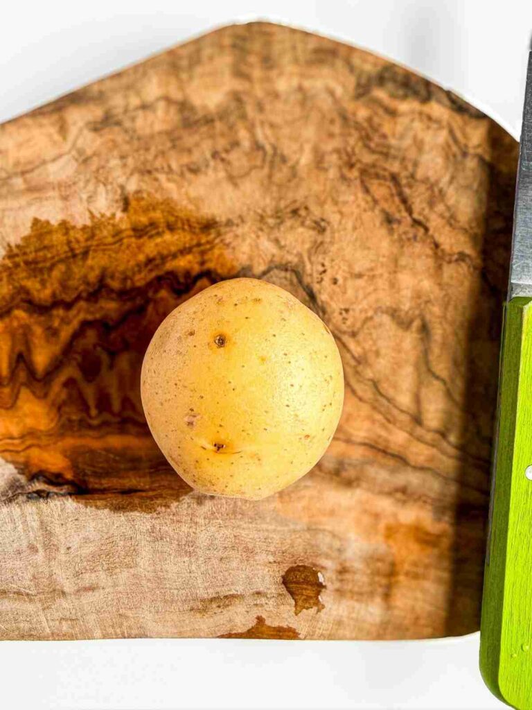 a potato on a cutting board for Crispy Potatoes with Everything Dill Tahini 