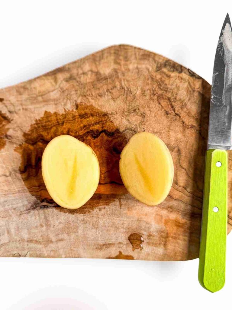 potato in half on a wooden cutting board for Crispy Potatoes with Everything Dill Tahini 