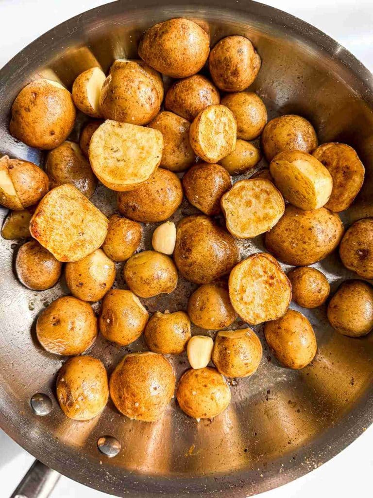 overhead view of seared baby poatatoes in a frying pan for pot roast chicken tomato broth.